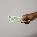A hand holding a twenty dollar bill against a plain gray background.