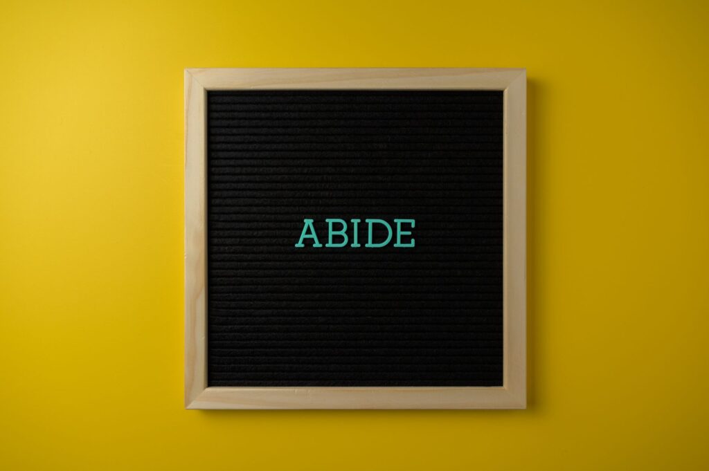 A black letter board with the word 'ABIDE' in teal on a vibrant yellow background, perfect for inspiration.