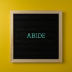 A black letter board with the word 'ABIDE' in teal on a vibrant yellow background, perfect for inspiration.