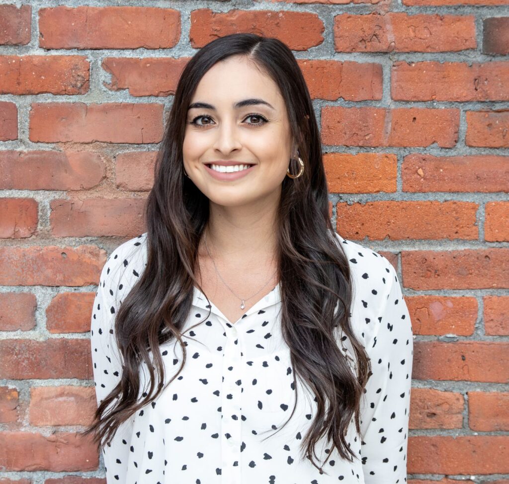 Confident woman posing in front of a brick wall, exuding professionalism.