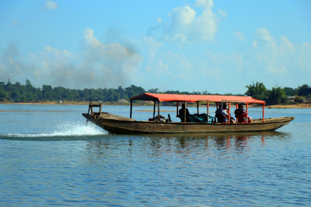 A traditional boat transporting people across a river in Sylhet, Bangladesh, under clear blue skies.