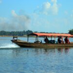 A traditional boat transporting people across a river in Sylhet, Bangladesh, under clear blue skies.