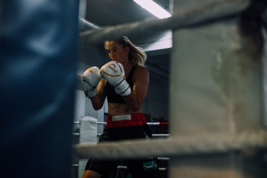A determined female boxer in athletic stance at a boxing gym.