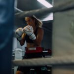 A determined female boxer in athletic stance at a boxing gym.