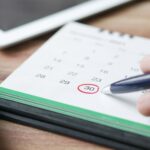 Close-up shot of a hand marking a date on a calendar with a pen, emphasizing planning and scheduling.