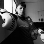 Black and white portrait of a female boxer with gloves and championship belt in a Buenos Aires gym.