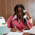 Professional woman in 80s style business attire making notes during a phone call.