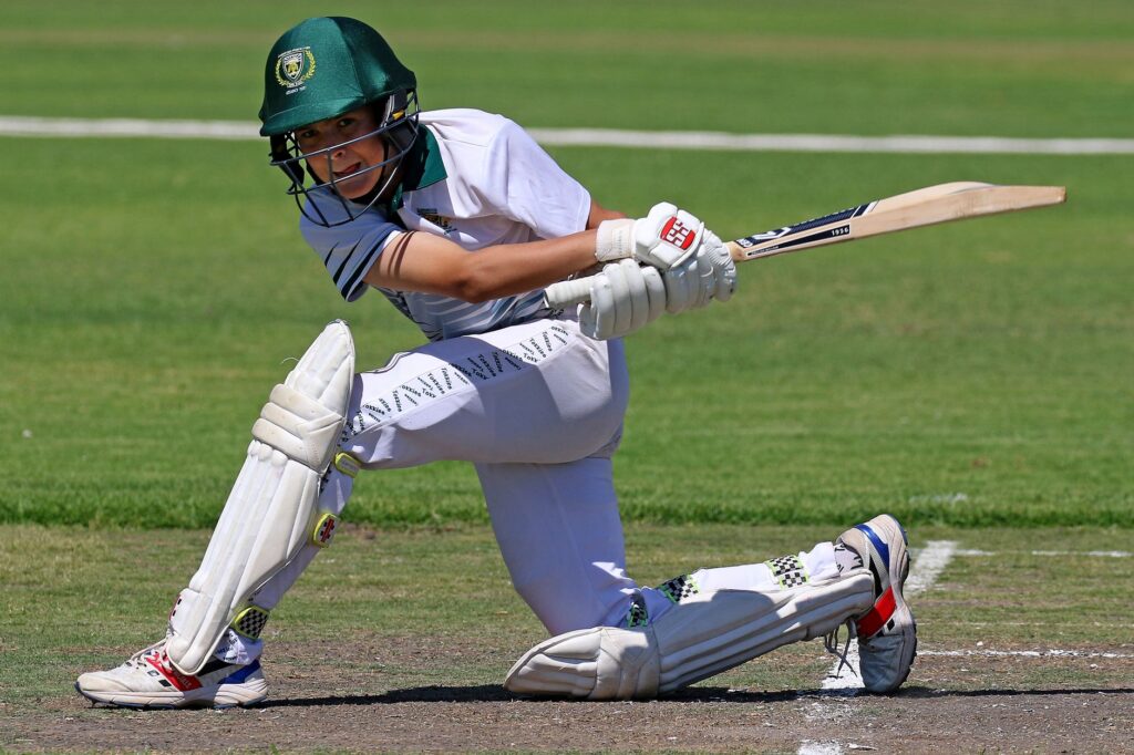 Dynamic action shot of a young cricket player batting on a grassy field.