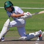 Dynamic action shot of a young cricket player batting on a grassy field.