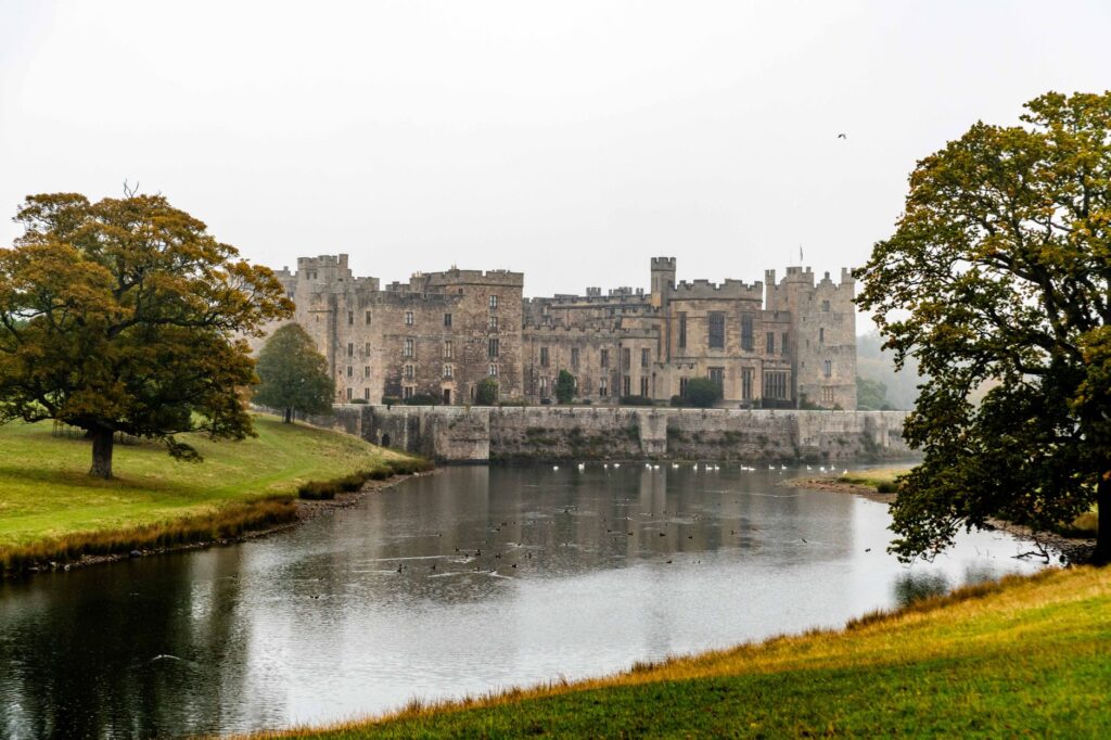 View of Raby Castle reflecting in a tranquil lake surrounded by lush green landscape.