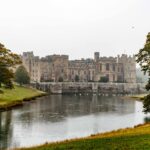 View of Raby Castle reflecting in a tranquil lake surrounded by lush green landscape.