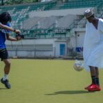 Two young men enjoy a casual soccer game in traditional attire at an Abuja stadium.