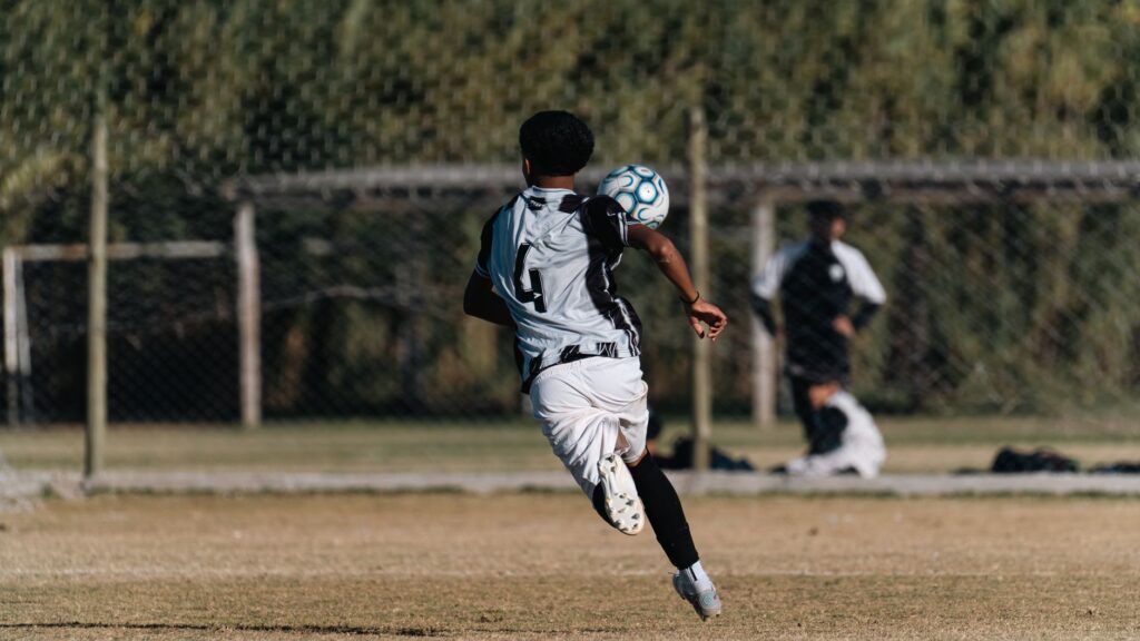 A young soccer player heads a ball during a game on a sunny outdoor field.