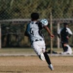 A young soccer player heads a ball during a game on a sunny outdoor field.