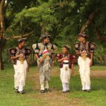 Men and boy in traditional Kandyan dress in a lush park setting, Sri Lanka.