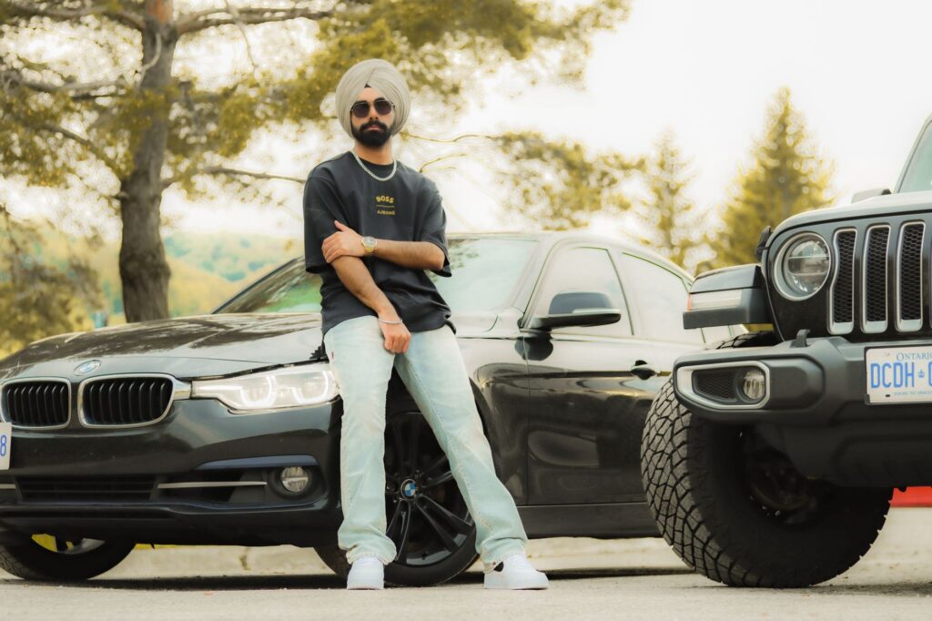 Man with turban and sunglasses striking a pose between a BMW and Jeep outdoors.