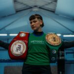 Female boxer poses with championship belts in an indoor boxing gym in Buenos Aires.