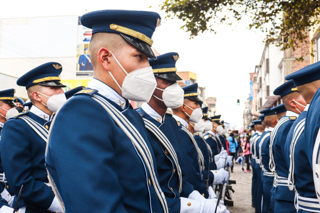 Soldiers in ceremonial uniforms wearing face masks marching in a parade on a street in Ecuador.