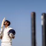 Cricket player in uniform celebrating a game-winning shot by kissing his bat on a sunny day.