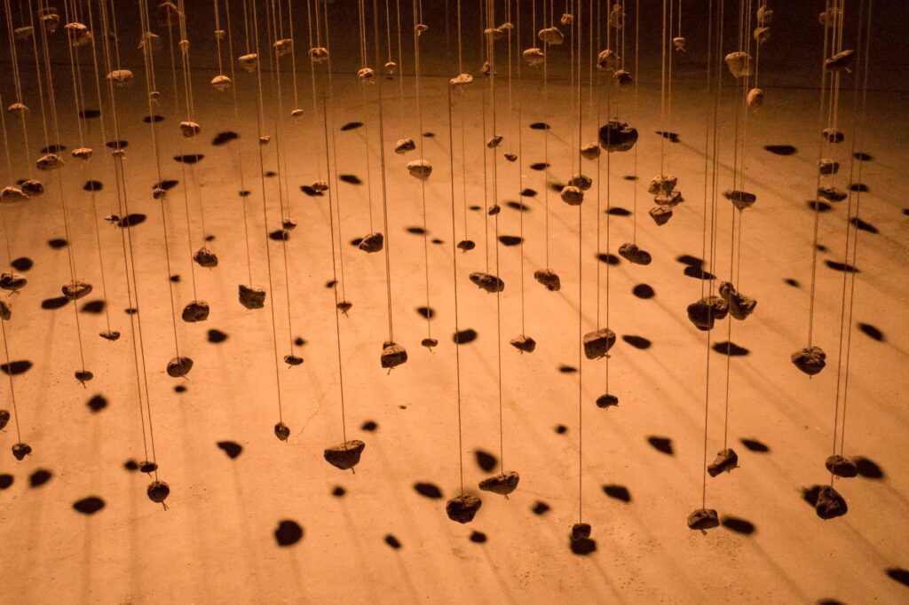 Creative installation of rocks suspended from strings casting striking shadows.