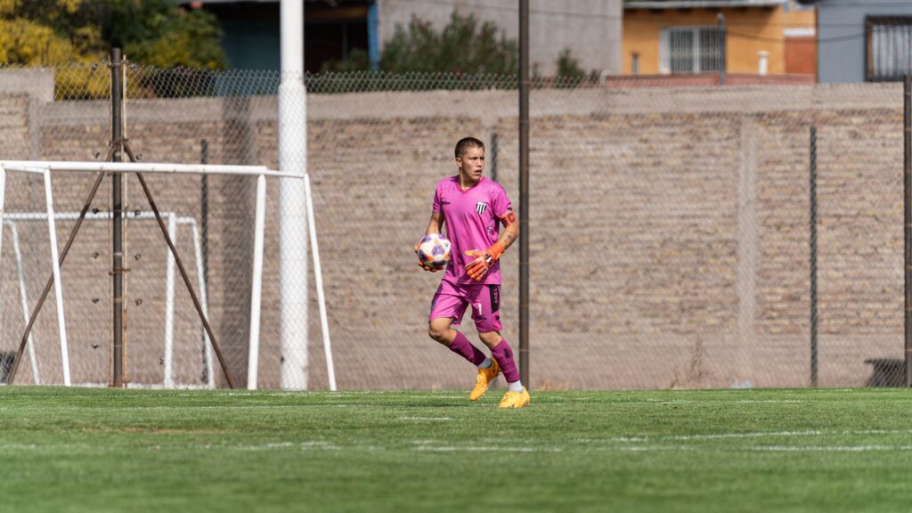 Goalkeeper in pink uniform catching a soccer ball during outdoor match.