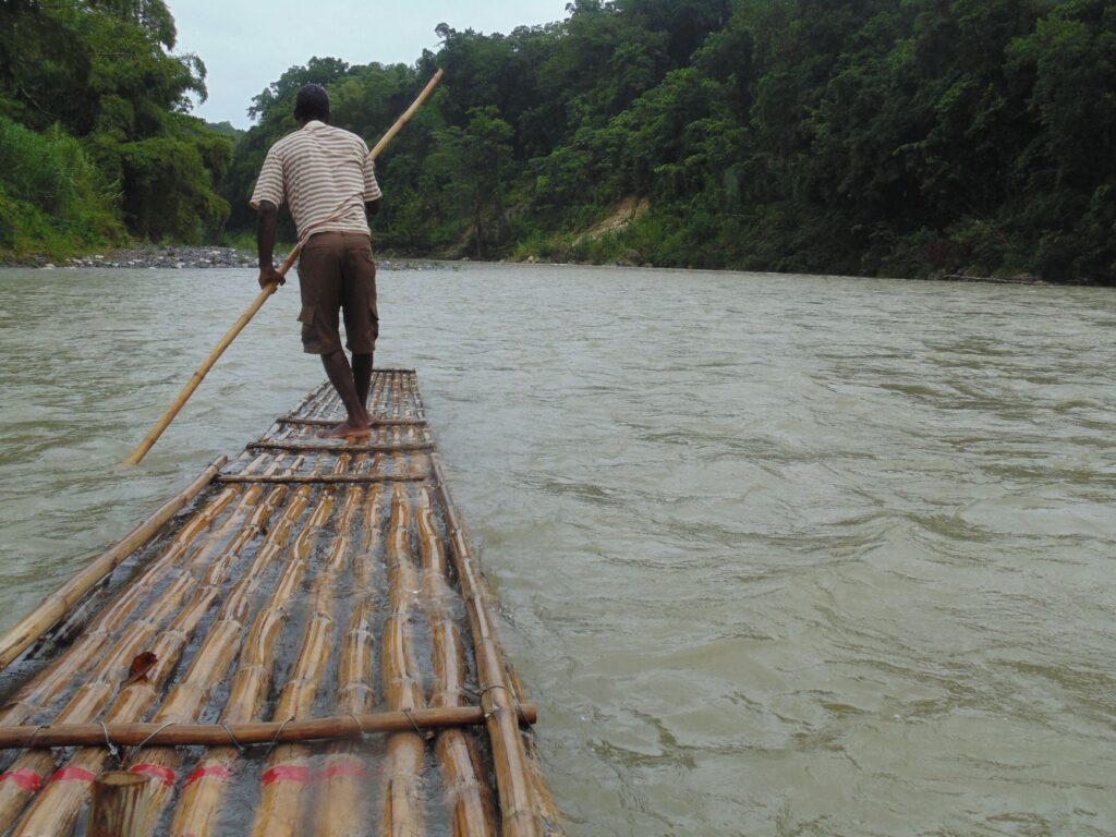 Man navigating a bamboo raft on the Rio Grande River in the lush landscape of Portland Parish, Jamaica.