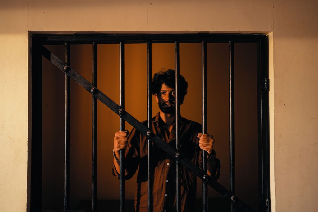 Portrait of a man standing behind bars in dramatic warm lighting. Captivating and intense.
