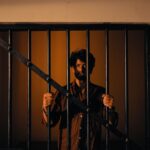 Portrait of a man standing behind bars in dramatic warm lighting. Captivating and intense.