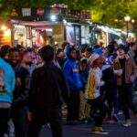 A lively crowd gathers around vibrant food trucks at night, enjoying a bustling street food experience.