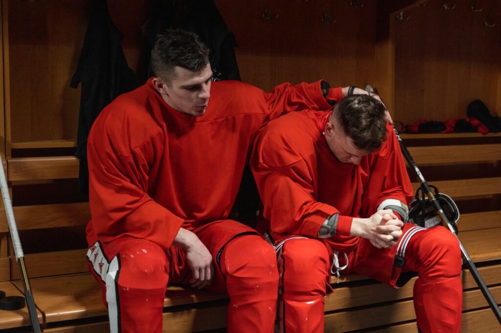 Two male hockey players share a moment of reflection in the locker room after a game.