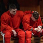Two male hockey players share a moment of reflection in the locker room after a game.
