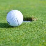A close-up image of a golf ball near a hole on a vibrant green golf course.
