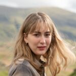 A woman with blonde hair poses in the windy hills of Windermere, England.