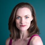 Portrait of a confident woman with blue eyes and brown hair against a teal background.