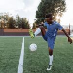 Young football player practicing tricks with a soccer ball on a sunny day outdoors.