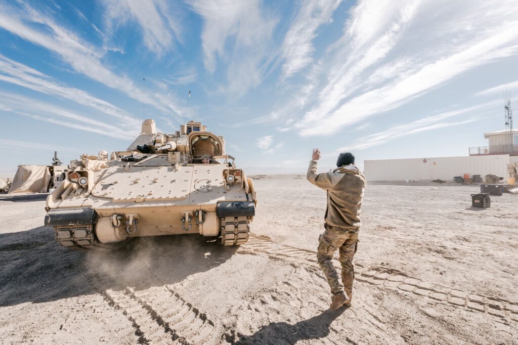 Bradley Fighting Vehicle and soldier in desert training operation under clear sky.