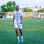 Soccer player in white kit on field, ready for action. Bright day outdoor sports scene.