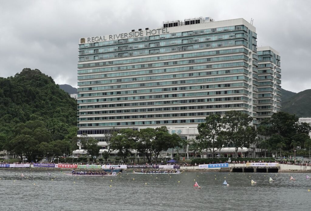 Panoramic view of Regal Riverside Hotel with a dragon boat race on the Shing Mun River in Hong Kong.