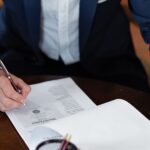 A professional individual signs legal documents at a desk in an office setting.