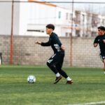 Two young men playing soccer on a field during a training session.