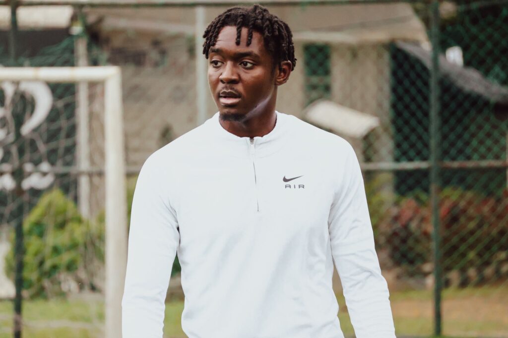 A young man in a white Nike jersey at an outdoor soccer field during the day.
