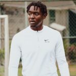 A young man in a white Nike jersey at an outdoor soccer field during the day.