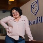 Plus-size woman smiling confidently with eyeglasses and pink shirt in an office.