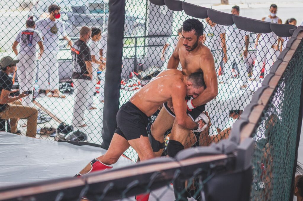 Two male MMA fighters engaging in an intense training session inside a gym cage.