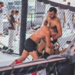 Two male MMA fighters engaging in an intense training session inside a gym cage.