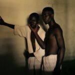 Two men in expressive poses captured in warm, dramatic lighting indoors.