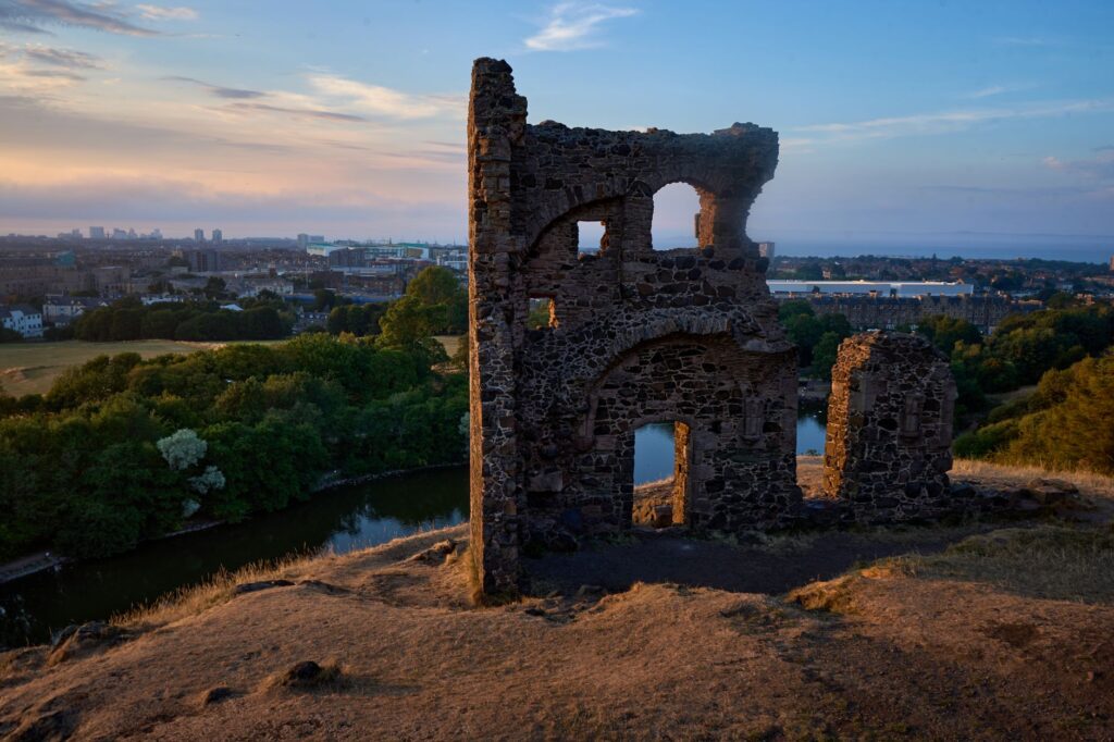 St. Anthony's Chapel ruins overlooking Edinburgh at sunset, captured from a hillside view.