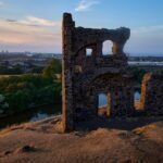 St. Anthony's Chapel ruins overlooking Edinburgh at sunset, captured from a hillside view.