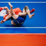 Two athletes engaged in an intense wrestling match on a blue mat.