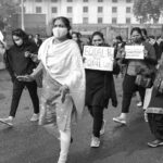 A black and white image of a women's rally advocating for equal pay, with participants wearing face masks and holding placards.
